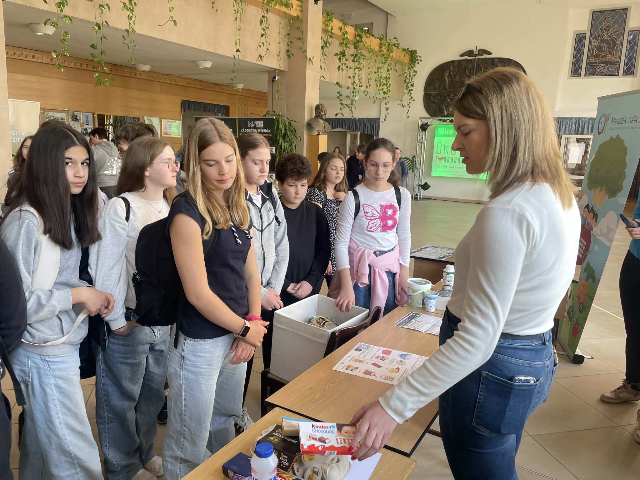A Nébih Oktatás kollégája gyermekekkel beszélget, akik különböző élelmiszerek csomagolásait figyelik meg.